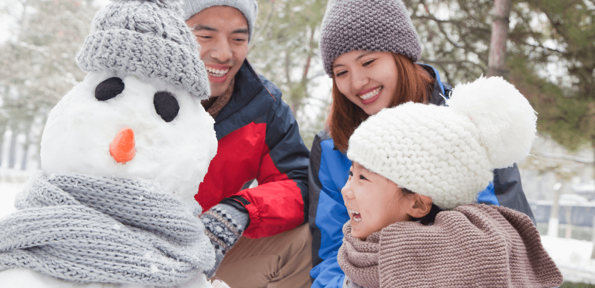 A family engaging in community-building winter activities like snowman building