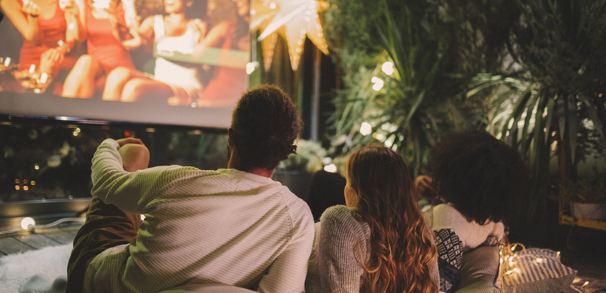 a couple cuddle on a blanket in front of a projector for an outdoor movie night